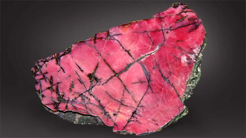 蔷薇辉石具有晶体结构，带有黑色包裹体，类似于贯穿石头的静脉
